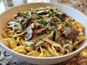 A close-up of a bowl of creamy beef stroganoff served over wide egg noodles, garnished with fresh parsley.