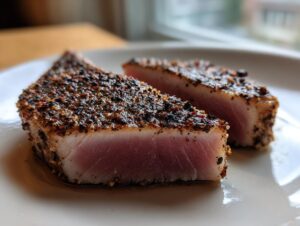 Two perfectly cooked slices of Blackened Tuna Steak on a white plate, showcasing the seared crust and pink interior.