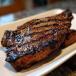 Close-up of a grilled steak with grill marks, glistening with a rich carne asada marinade.