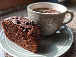 A slice of moist Cottage Cheese Microwave Brownie topped with chocolate chips, served next to a cup of coffee.
