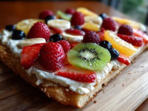 A close-up of a vibrant fruit pizza sugar cookie slice topped with cream cheese frosting and fresh strawberries, kiwi, blueberries, raspberries, and banana.