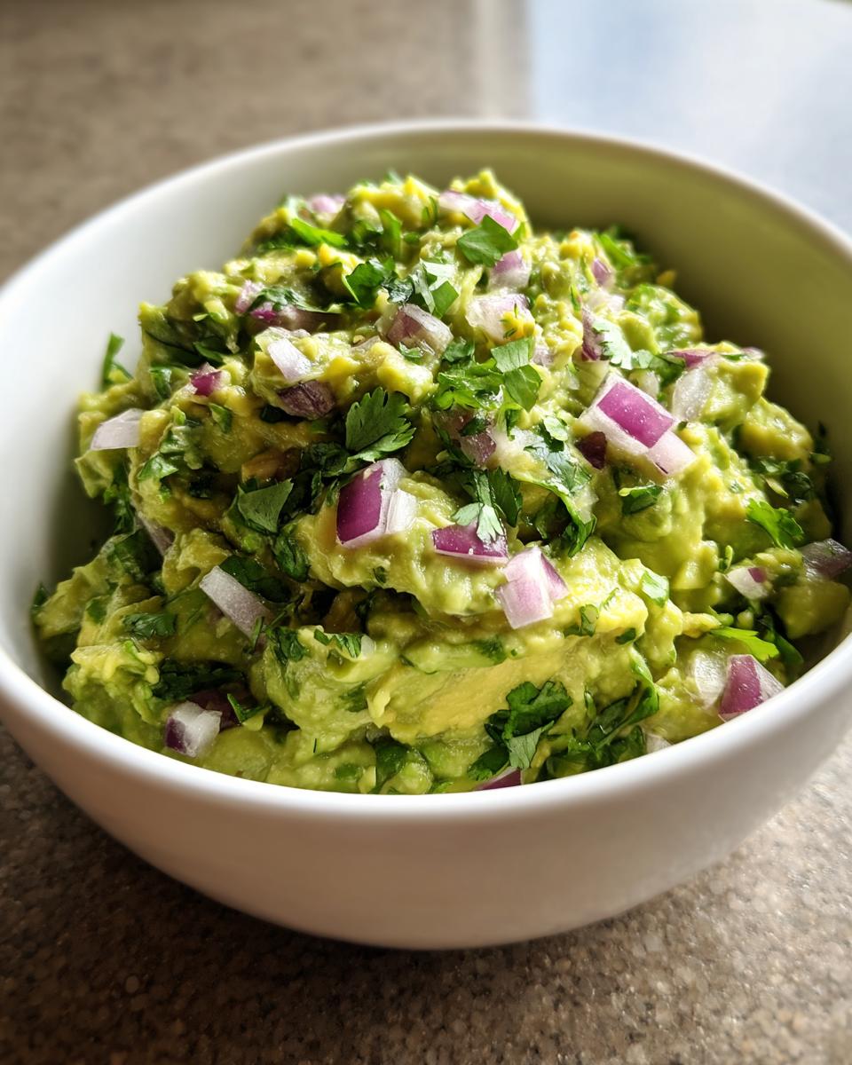 A bowl of chunky Homemade Guacamole, topped with diced red onion and fresh cilantro.
