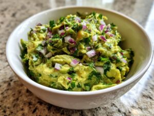 A bowl of chunky Homemade Guacamole topped with diced red onion and fresh cilantro.