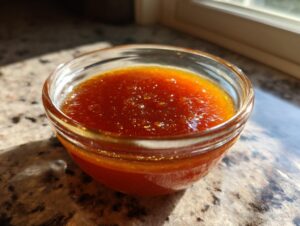 A close-up of a clear glass bowl filled with rich, amber-colored honey BBQ sauce.