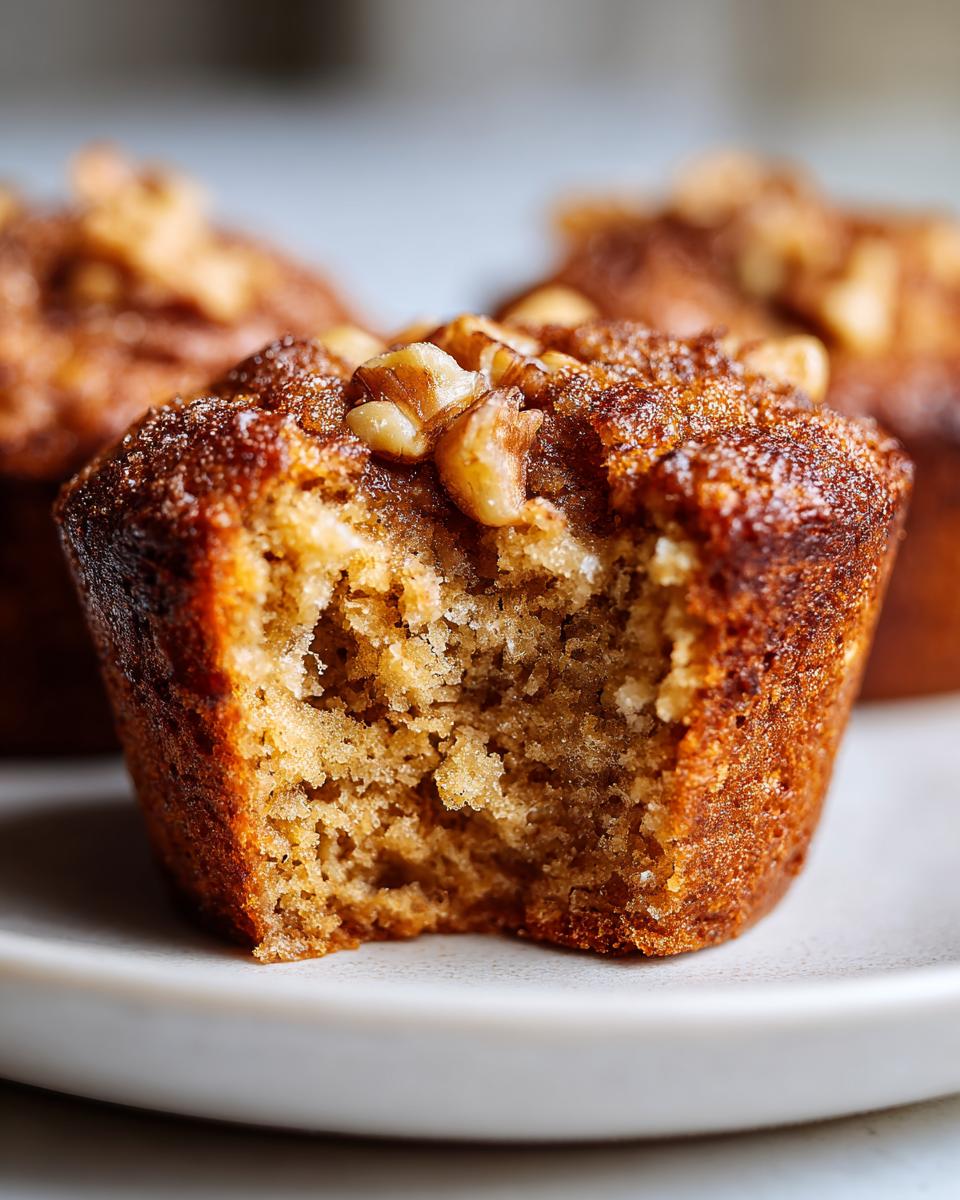 Close-up of a moist banana nut muffin with a bite taken out, showing a fluffy interior and topped with walnuts.