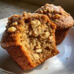 Close-up of a moist banana nut muffin, cut in half, showing chunks of walnuts and a sugary topping.