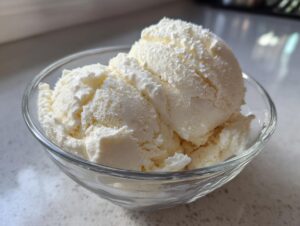 A clear glass bowl filled with creamy scoops of homemade protein ice cream.