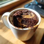 Close-up of a rich chocolate protein mug cake with a gooey peanut butter swirl, served in a white mug.