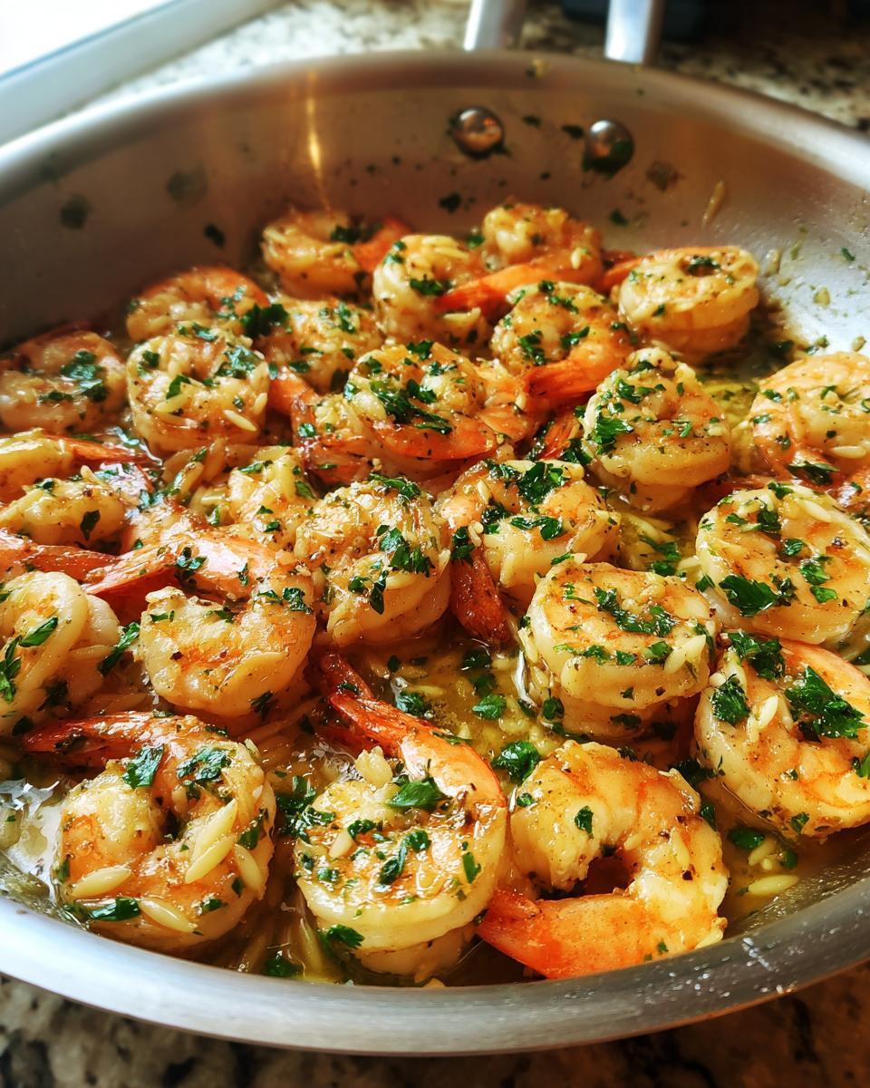Close-up of shrimp orzo in lemon garlic sauce, garnished with fresh parsley, in a stainless steel pan.