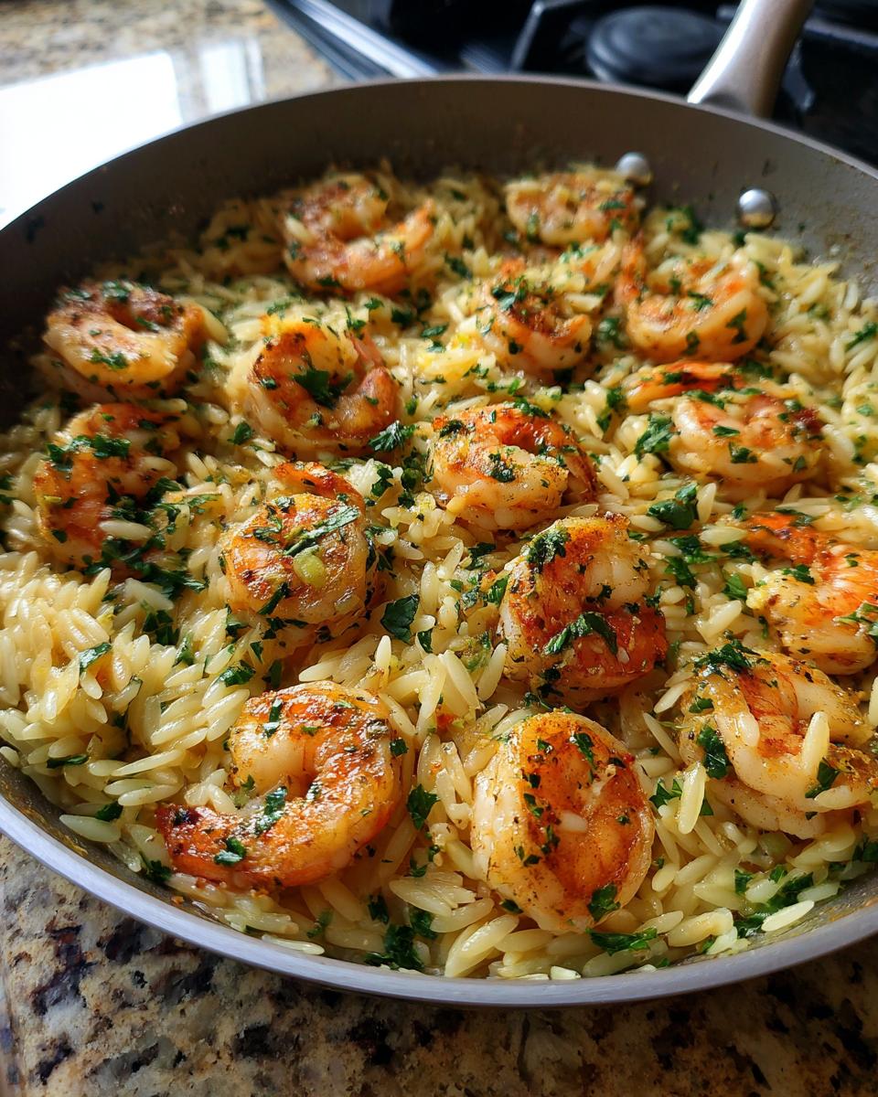 Close-up of a skillet filled with shrimp orzo in lemon garlic sauce, garnished with fresh parsley.