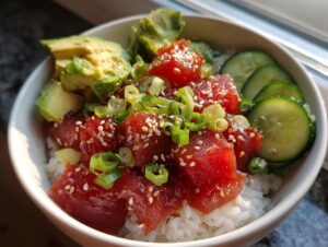 A close-up of a vibrant Tuna Poke Bowl, featuring fresh tuna cubes, avocado slices, cucumber, and green onions over rice.