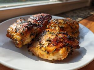 Four pieces of crispy, golden-brown air fryer Mediterranean chicken thighs seasoned with herbs on a white plate.