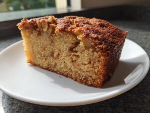 A close-up shot of a moist slice of apple cake with visible chunks of apple and a dark, caramelized top crust.