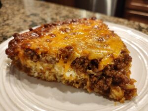 A close-up slice of baked beans and ground beef casserole topped with melted cheddar cheese.
