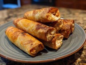 A stack of golden-brown baked chicken taquitos on a gray plate, showing the shredded chicken filling.