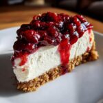 Close-up of a perfect slice of berry cheesecake with a thick graham cracker crust and glossy red berry topping.