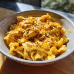 A close-up of a bowl filled with creamy cajun ranch chicken pasta, topped with herbs and spices.