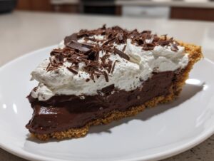 A decadent slice of Christmas chocolate cream pie featuring a thick chocolate filling, graham cracker crust, and topped with whipped cream and chocolate shavings.