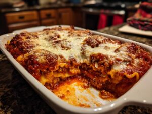 A close-up of a freshly baked Crockpot ravioli lasagna in a white baking dish, with melted cheese and rich tomato sauce.