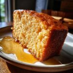A moist slice of Greek yogurt cake with honey syrup drizzled over it, served on a plate.
