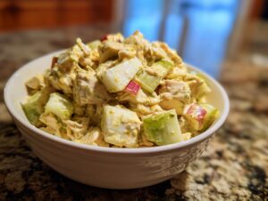A bowl of creamy honey mustard chicken salad with chunks of chicken, apple, and celery.