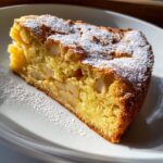 Close-up of a moist slice of Italian apple cake, studded with apple pieces and dusted with powdered sugar.