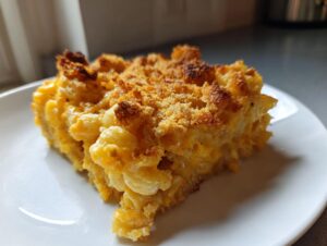A close-up of a square serving of creamy Million Dollar Mac and Cheese with a golden, crispy baked topping.