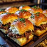 Close-up of delicious Mississippi Pot Roast Sliders on a baking sheet, topped with fresh herbs.
