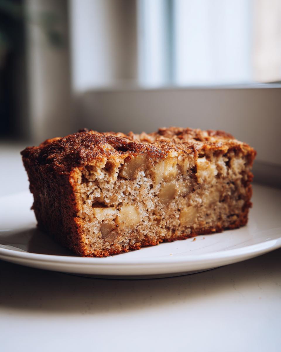 Close-up of a thick slice of moist apple cake, showing chunks of apple and a cinnamon sugar crust.
