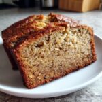 Close-up of two moist banana bread slices on a white plate, showcasing the texture and brown crust.