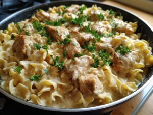 Close-up of one-pan chicken and buttered noodles in a skillet, garnished with fresh parsley.