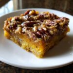 A close-up, appetizing slice of pumpkin dump cake topped generously with glazed pecans on a white plate.