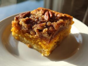 Close-up of a square slice of rich, orange pumpkin dump cake with a crumbly, pecan-topped crust.