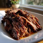 Close-up of tender, shredded Slow Cooker Beef Brisket glistening with sauce on a white platter.