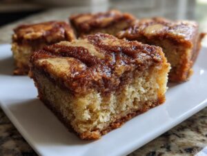 A close-up of a square snickerdoodle blondies piece showing a moist, cake-like interior and a rich, cinnamon-swirled topping.