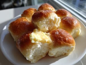 A plate of freshly baked, golden brown Texas Roadhouse rolls, one split open with melting butter.