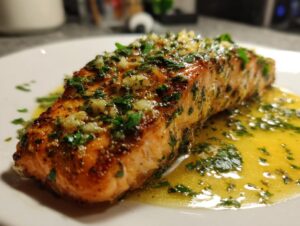Close-up of a juicy air fryer salmon fillet topped with minced garlic and parsley, resting in a pool of melted butter sauce.