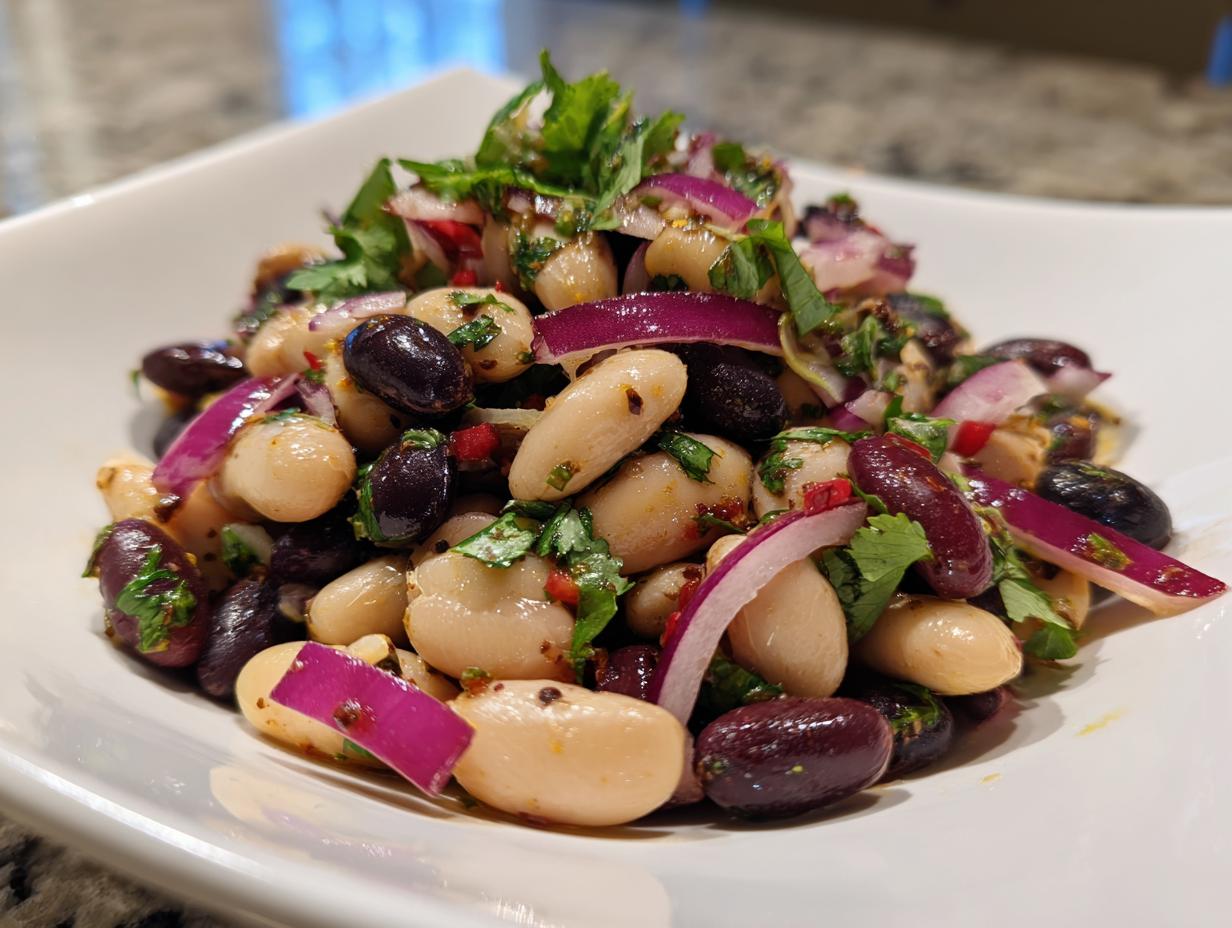 A vibrant close-up of a mixed bean salad featuring white beans, black beans, red onion slices, and cilantro.