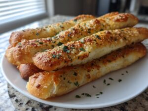 A stack of freshly baked, golden brown garlic breadsticks topped with melted cheese and parsley.