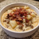 A close-up of a bowl of rich cheeseburger soup recipe, featuring ground beef, potato chunks, and crumbled bacon topping.