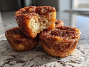 A stack of three golden brown french toast muffins, one cut open to show the soft interior.