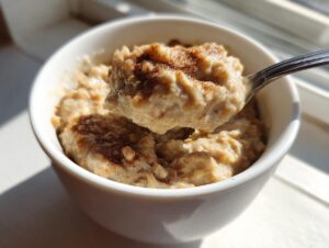 A spoonful of creamy banana oatmeal topped with cinnamon being lifted from a white bowl.