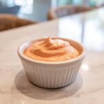 Close-up of creamy, orange-colored burger sauce swirled high in a small white ramekin.