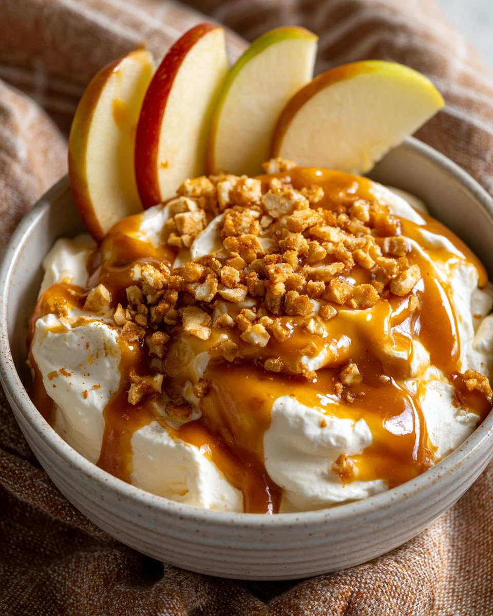 Close-up of a creamy apple dip topped with caramel sauce and chopped nuts, served with fresh apple slices.