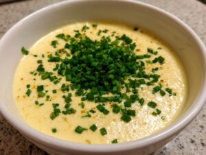 Close-up of a bowl of creamy, yellow cauliflower soup garnished generously with chopped green chives.