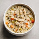 Overhead view of a creamy chicken wild rice soup featuring shredded chicken, carrots, and celery in a white bowl.