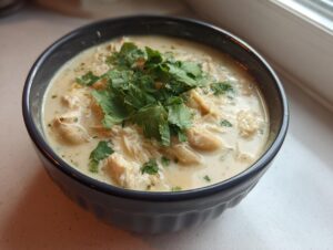 A close-up of a creamy white chicken chili recipe topped generously with fresh cilantro in a dark blue bowl.