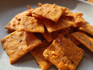 Close-up of a pile of homemade, crispy orange cheese crackers sprinkled with coarse salt.