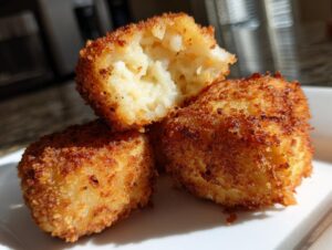 Close-up of three golden brown, crispy potato croquettes stacked, one cut open revealing the soft, mashed potato filling.