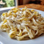Close-up of fettuccine pasta generously coated in creamy homemade alfredo sauce and topped with cracked black pepper.